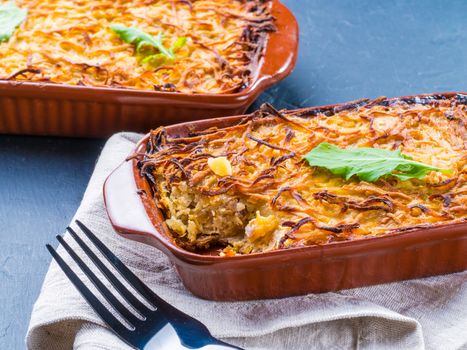 Close up view of appetizing potato casserole with fish, eggs and cream. Potato casserole in serving baking dish on dark concrete background