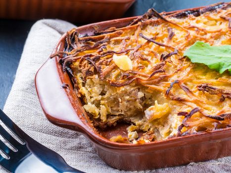 Close up view of appetizing potato casserole with fish, eggs and cream. Potato casserole in serving baking dish on dark concrete background