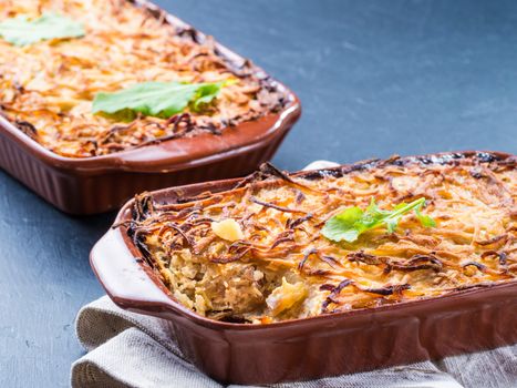 Close up view of appetizing potato casserole with fish, eggs and cream. Potato casserole in serving baking dish on dark concrete background