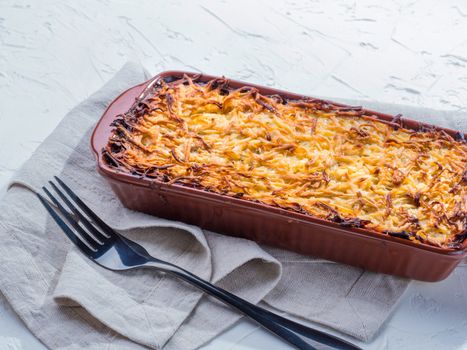 Close up view of appetizing potato casserole with fish, eggs and cream. Potato casserole in serving baking dish on white concrete background