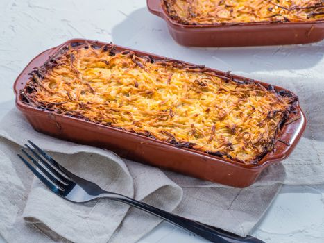 Close up view of appetizing potato casserole with fish, eggs and cream. Potato casserole in serving baking dish on white concrete background