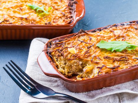 Close up view of appetizing potato casserole with fish, eggs and cream. Potato casserole in serving baking dish on dark concrete background