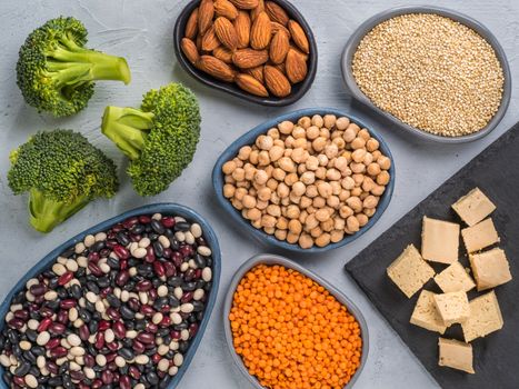 Vegetarian healthy protein sources on gray concrete background. Quinoa, chickpea, almond, red lentils, mixed bean, broccoli, tofu as vegan sources of protein concept. Close up. Top view or flat lay.