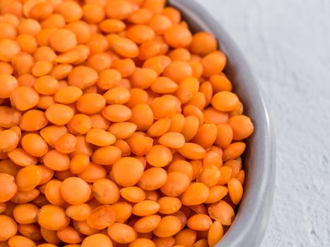 Extreme close up view of raw orange or red lentils in gray plate on gray concrete background. Copy space.