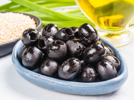 Close up view of black olives in blue plate on gray concrete background. Olive oil, green onion and quinoa in background