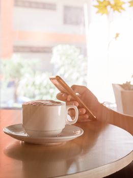 Hand woman using smartphone in coffee shop and a cup of coffee on the table with soft light vintage filter