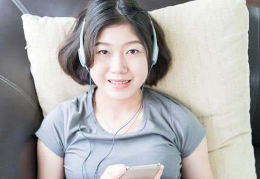 Close up young asian woman short hair listening music from mobile phone on the couch