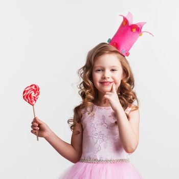 Beautiful little candy princess girl in crown holding big pink heart lollipop and smiling