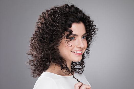 Portrait of amazing beautiful smiling woman with curly hair on gray background with copy space