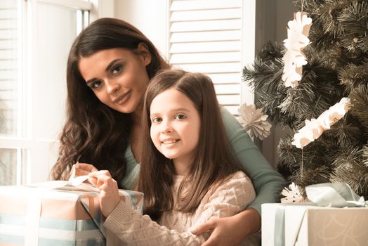 Mother and daughter unwrapping a gift sitting on the floor near christmas tree