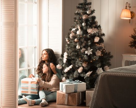 Mother and daughter unwrapping a gift sitting on the floor near christmas tree