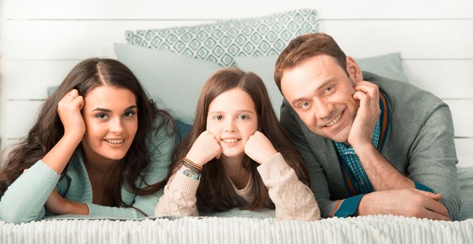 Family portrait of happy parents and their daughter laying on bed at home