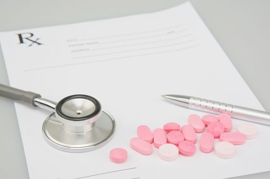 Close up old silver medical stethoscope and pink pills have blur silver pen and rx prescription form as background on white table and copy space. Healthcare and medical concept photography.