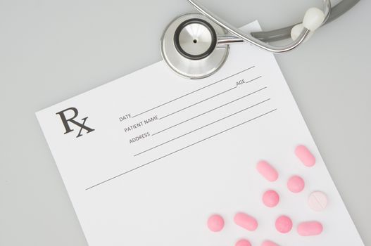 Old silver medical stethoscope and pink pills place on rx prescription form with white background and copy space. Healthcare and medical concept photography.