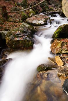 Rapids and waterfall in the mountains in autumn forest with yellow, orange foliage, boulders and rocks covered with moss, Bistriski Vintgar, Slovenia