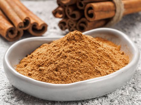 Close up view of ground cinnamon in trendy plate and cinnamon sticks on gray cement background