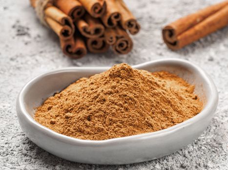 Close up view of ground cinnamon in trendy plate and cinnamon sticks on gray cement background