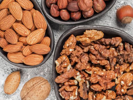 Walnuts, almonds and hazelnuts in trendy plates on gray cement background. Top view or flat lay.