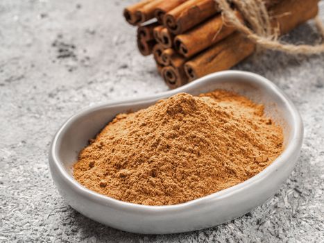 Close up view of ground cinnamon in trendy plate and cinnamon sticks on gray cement background