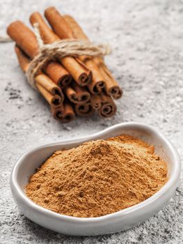 Close up view of ground cinnamon in trendy plate and cinnamon sticks on gray cement background. Vertical.