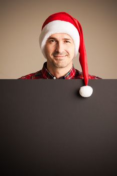 Man wearing santa christmas hat holding and pointing blank billboard or placard sign copy space for text advertising