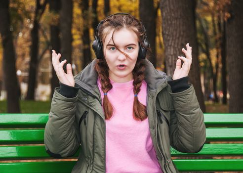 Surprised young girl with headphones. A teenage girl on a park bench in autumn.