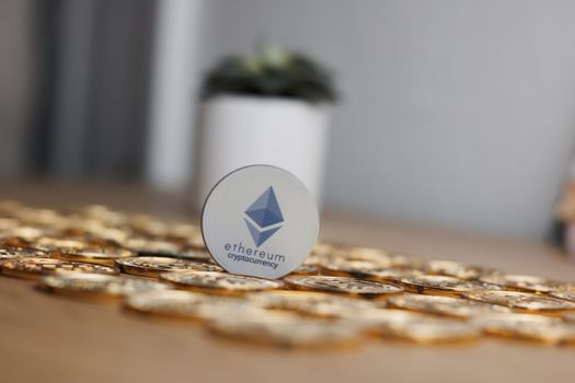 Digital currency physical grey ethereum token on gold bitcoin coins near flower.