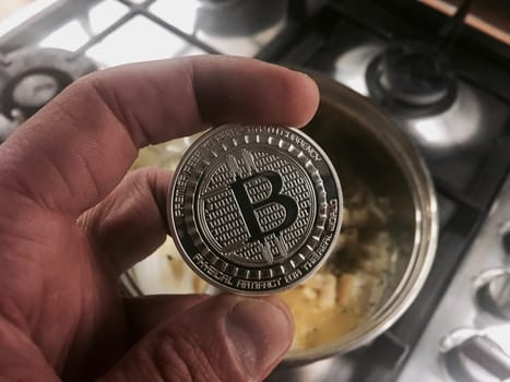 Crypto currency physical metal silver bitcoin coin in hand near the kitchen.