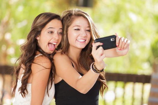 Two Attractive Mixed Race Girlfriends Using Their Smart Cell Phones For Selfie Outdoors