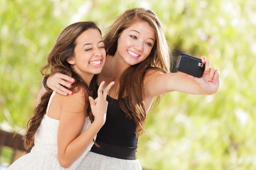 Two Attractive Mixed Race Girlfriends Using Their Smart Cell Phones For Selfie Outdoors