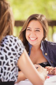 Two Mixed Race Girlfriends Having A Conversation At An Outoor Patio Table