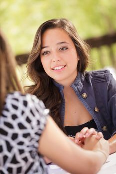 Two Mixed Race Girlfriends Having A Conversation At An Outoor Patio Table