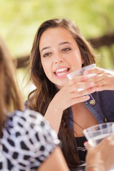 Expressive Young Adult Woman Having Drinks and Talking with Her Friend Outdoors