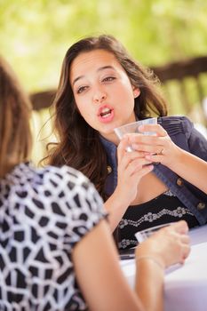 Expressive Young Adult Woman Having Drinks and Talking with Her Friend Outdoors