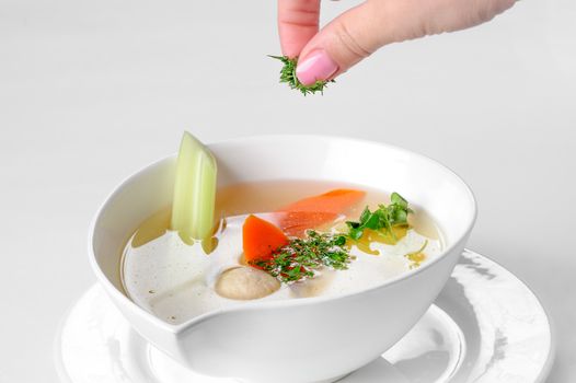 portion of soup with meatballs and vegetables, human hand with greens