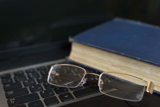 Glasses and the book on the laptop's keyboard. Close up.