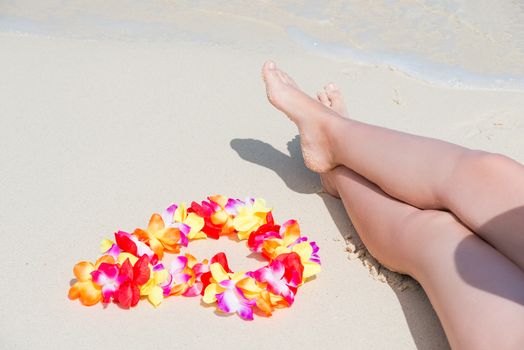 beautiful female legs on a sandy beach and Hawaiian Lei close-up