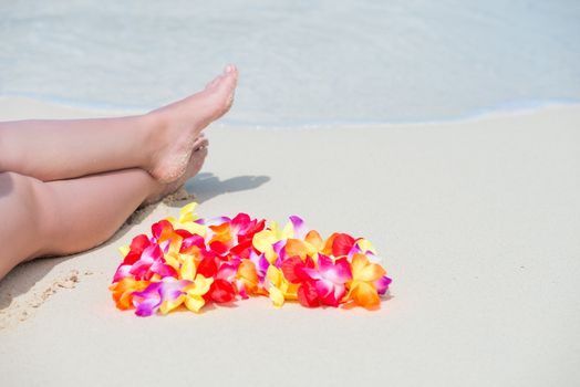 Hawaiian beads, floral lei and beautiful female legs on the beach in the sand