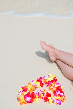 Hawaiian beads in the shape of a heart near the female legs on the beach view from above