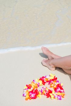 floral Hawaiian Lei in the shape of a heart near the female legs on the beach view from above