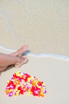 beautiful legs and Hawaiian floral lei near the sea on white gentle sand