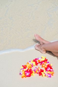 sea wave, female feet and floral Hawaiian beads on the ocean shore