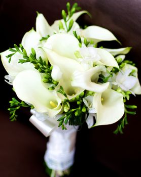Beautiful Bridal Bouquet with Callas, Snowdrops and Green Buds and Satin Ribbon closeup on Dark background. Focus on Pestle of Calla