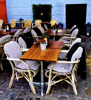 December Rustic Sidewalk Cafe with Wooden Tables, Flower Pot of Poinsettia and Plaids on Wicker Chair Outdoors