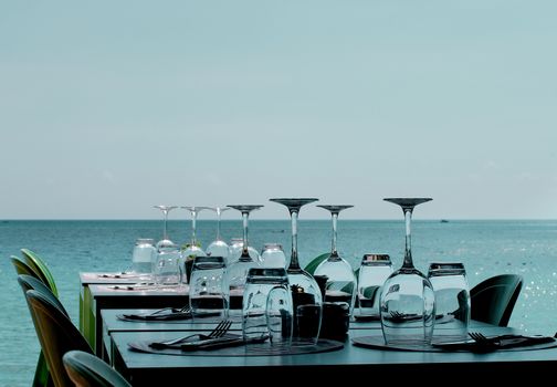 Elegant Restaurant Tables with Various Stemware and Silverware on Terrace in Shadow on Sea Coast Outdoors. Turquoise Toned