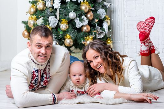 family with son near New Year's fir tree posing and lying on the floor