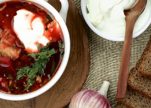 Ukrainian National Traditional Beet Soup Borscht with Brown Bread, Garlic and Sour Cream on Wooden Plate with Wooden Spoon. Top View