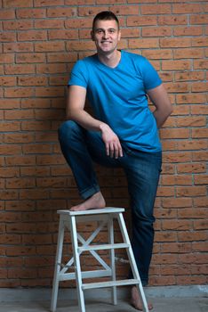 brutal barefoot man in a chair posing against a brick wall background