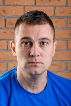 man brunet in blue t-shirt on brick wall background