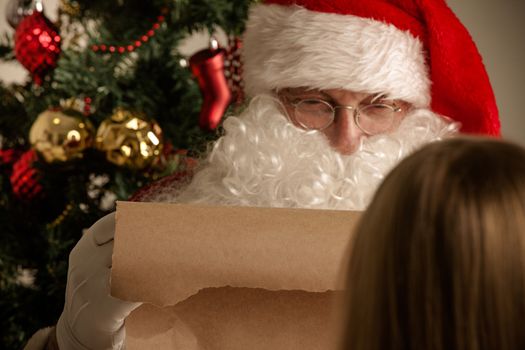 Santa Claus with with list or nice or naugthy list paper with small boy near christmas tree